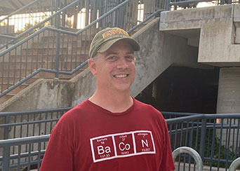 James Carsner outside smiling with a baseball cap and red shirt on. 